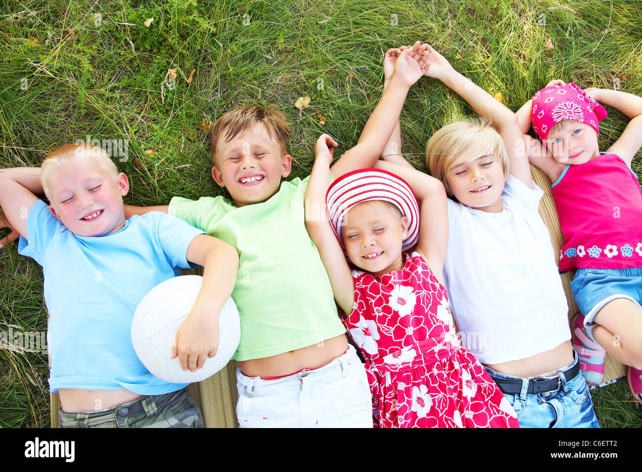 Fünf niedliche Kinder im grünen Rasen liegen und genießen im Sommer Stockfoto