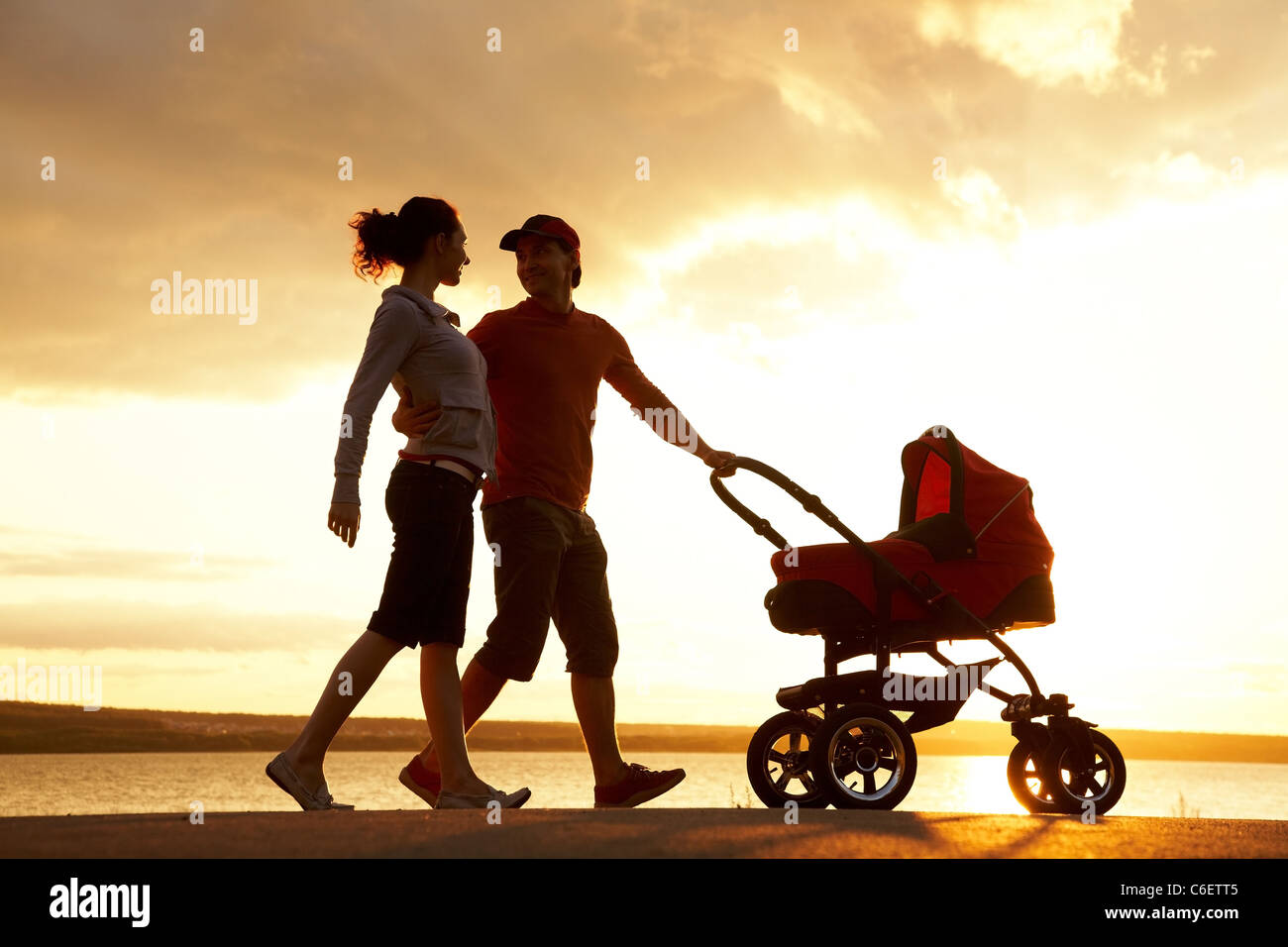 Silhouetten von glücklichen Eltern mit Kinderwagen zu Fuß an der Küste Stockfoto