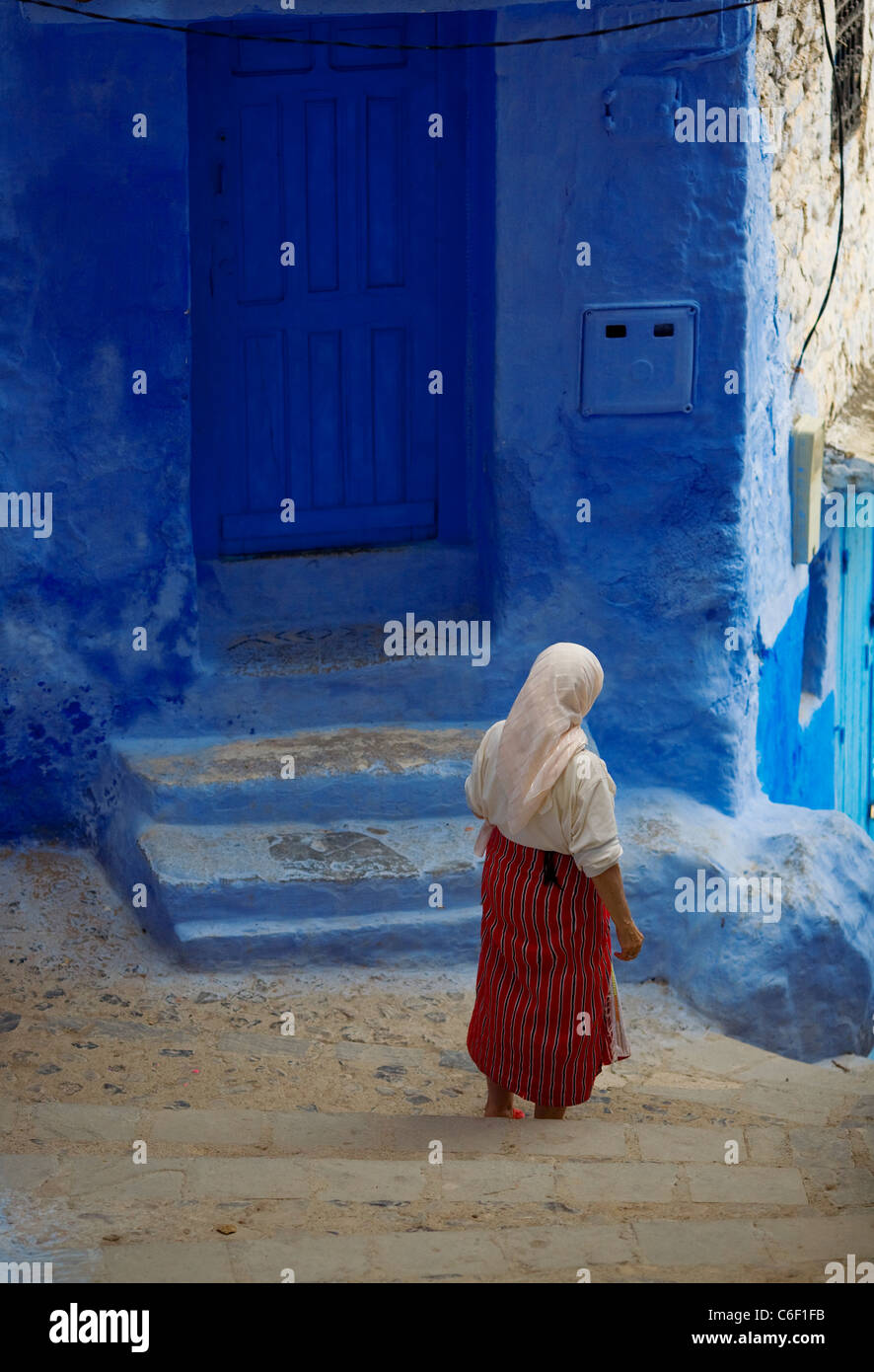 Frau zu Fuß vorbei an blauen Häusern und Gassen von Chefchaouen, Marokko Stockfoto