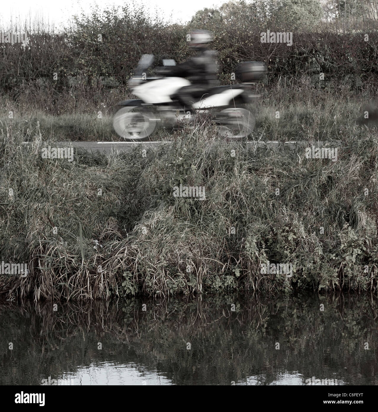 Ein weißer BMW Motorrad Reisen entlang einer Landstraße neben dem Nottingham Kanal, unscharf verschwommen, als es von Geschwindigkeiten. Stockfoto