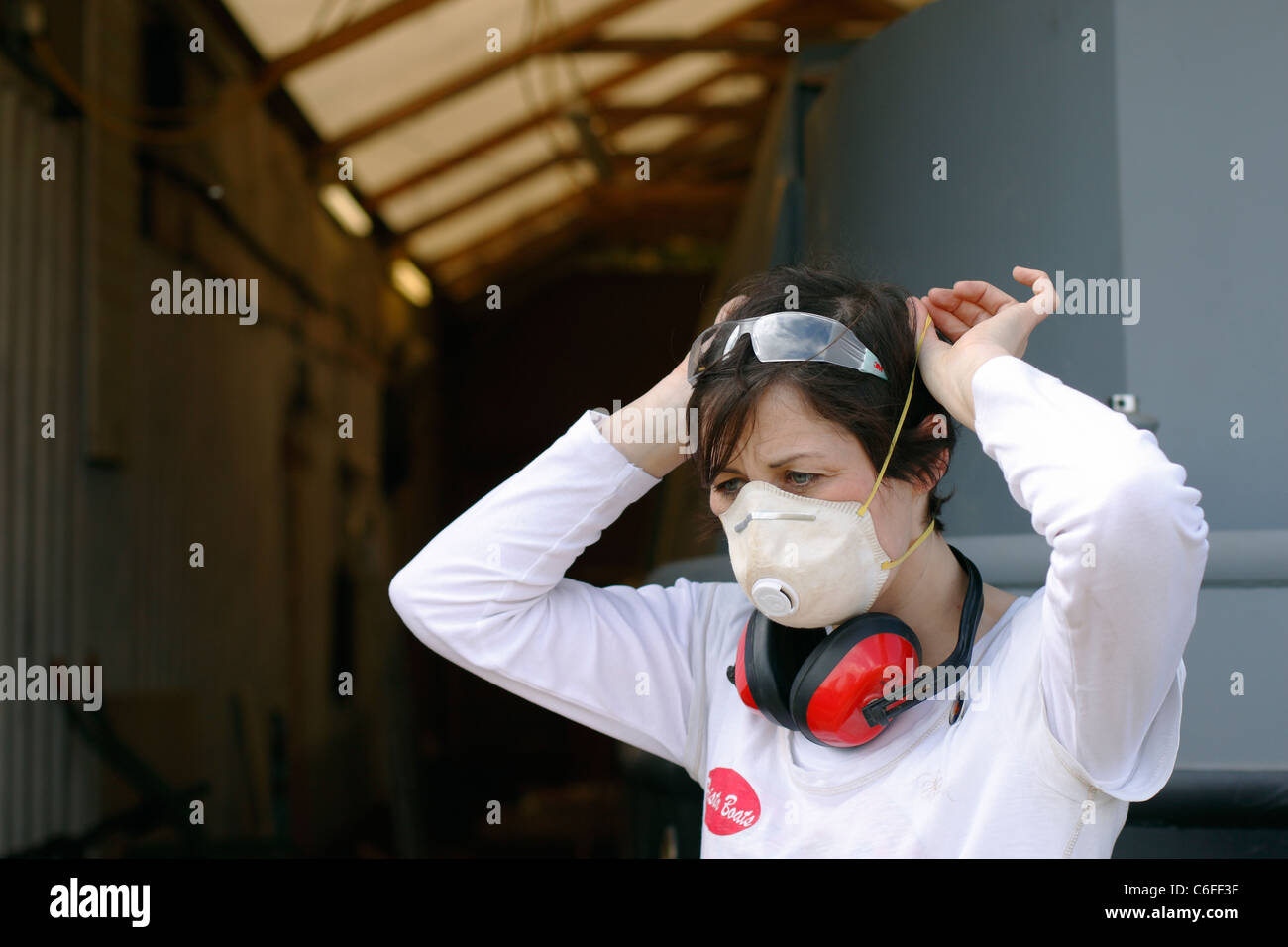 Eine junge Frau, die auf eine Gesichtsmaske, Schutzbrille Gehörschutz und Sicherheit zum Schutz während der Arbeit. Stockfoto