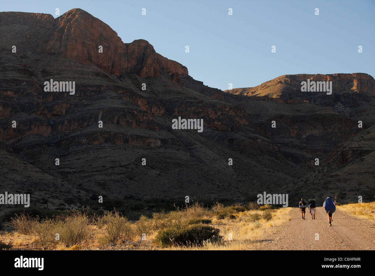 Drei Wanderer zu Fuß über eine Schotterstraße in Wüstenlandschaft Stockfoto