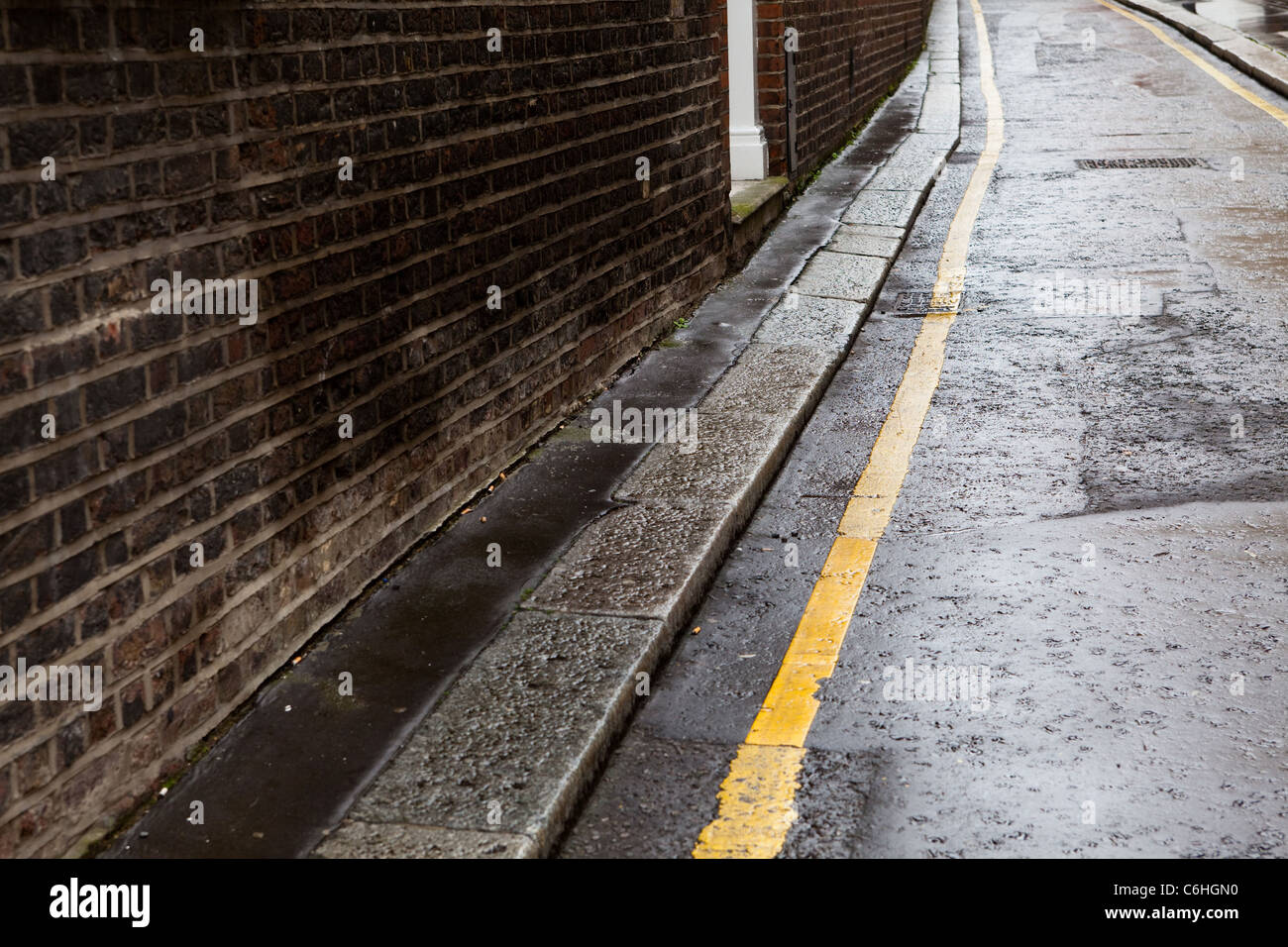 Einzelne gelbe Linie und Ziegel Wand auf einer Straße nass-Straße, nahe Chancery Lane, London Stockfoto