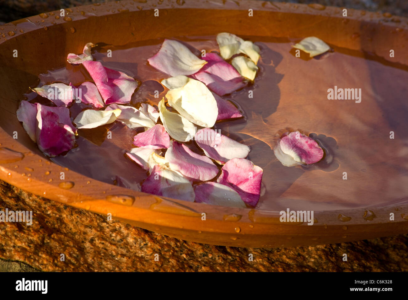 Rosenblätter schweben auf dem Wasser in einer Holzschale Stockfoto