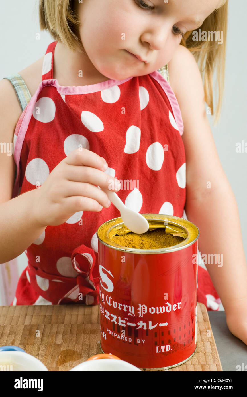 Kleines Mädchen schöpfen Currypulver aus Dose Stockfoto