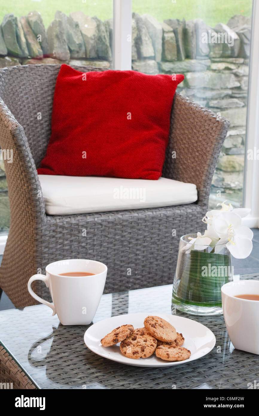 Kaffee und Gebäck in eine moderne, aber gemütliche Wohnlandschaft mit Korbmöbel in einem Wintergarten-Wohnzimmer Stockfoto