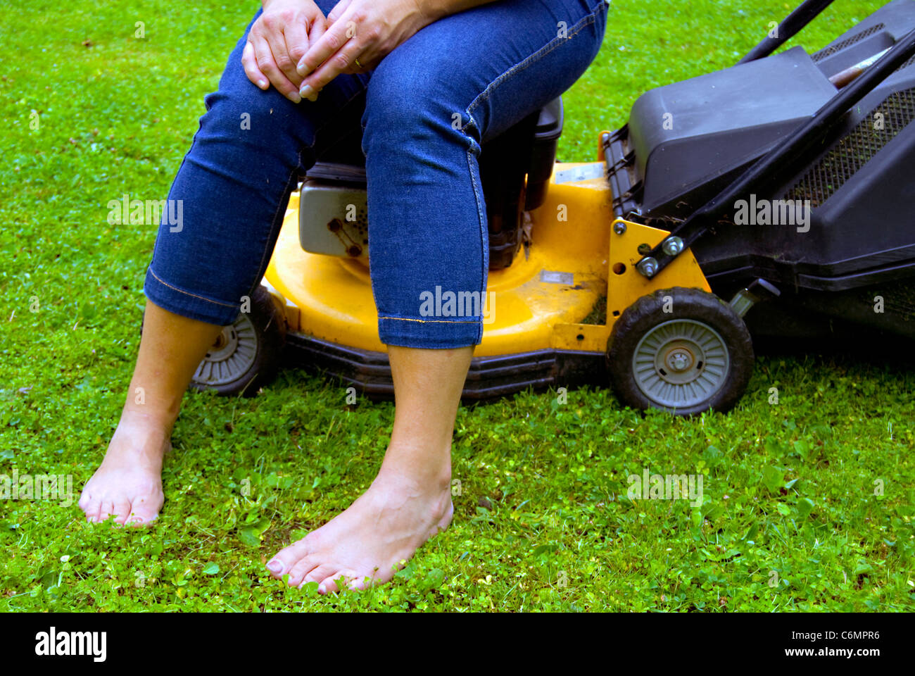 Frau nimmt sich eine Auszeit vom Gartenbau einerlei, sitzt auf einem Rasenmäher Stockfoto