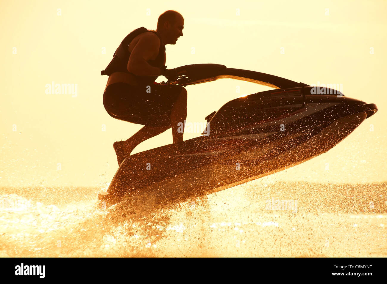 starker Mann springt auf dem Jetski über das Wasser im Sonnenuntergang .silhouette Spray. Stockfoto