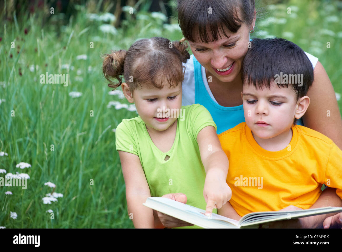 Junge Frau lesen zu buchen, kleines Mädchen und netten jungen auf einer Wiese Stockfoto