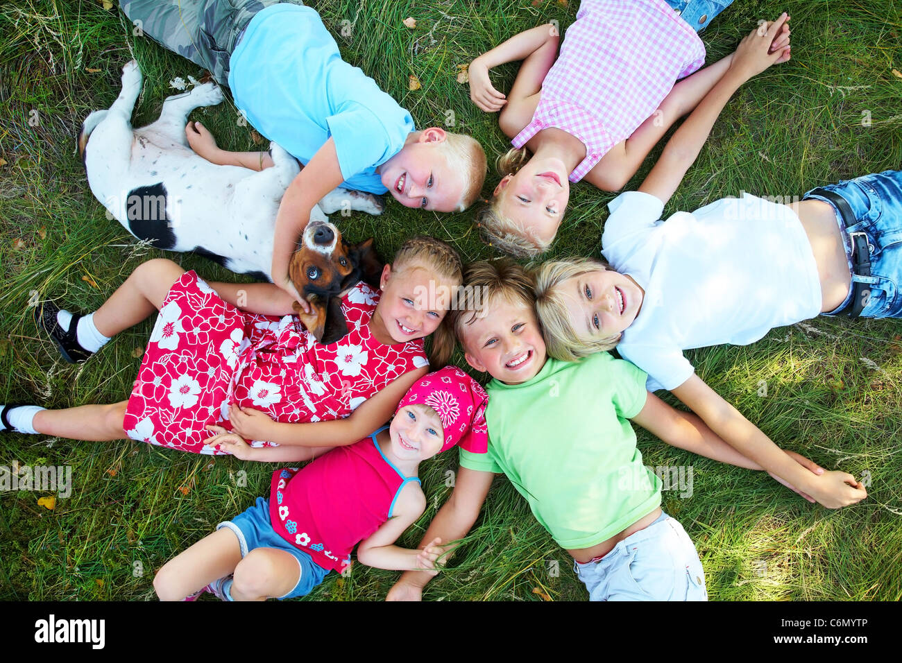 Sechs niedliche Kinder und Hund liegen im grünen Rasen und genießen im Sommer Stockfoto
