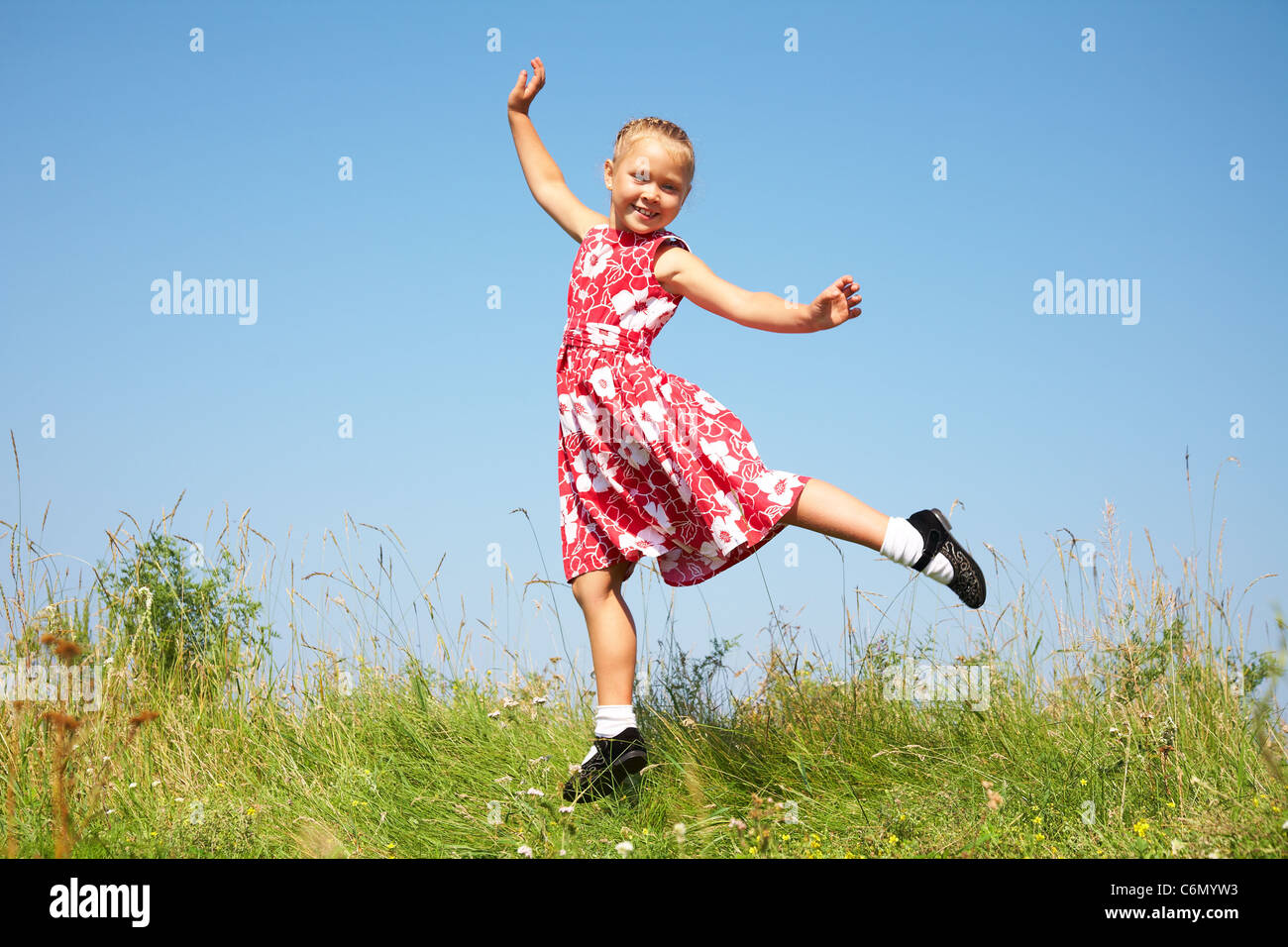 Niedliche Mädchen springen auf Sommerwiese gegen blauen Himmel Stockfoto