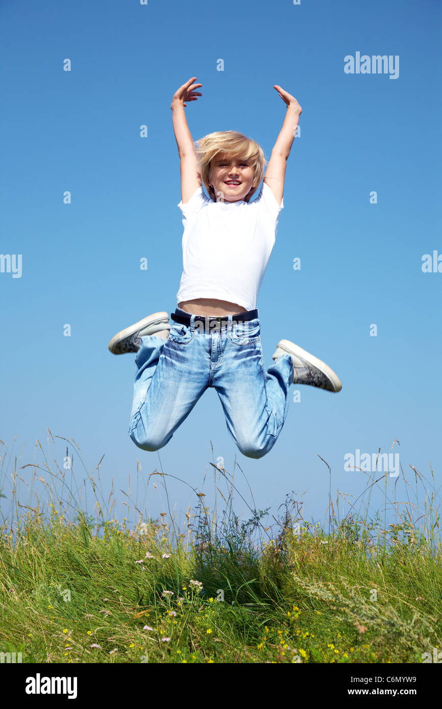 Süße junge springt auf Sommerwiese gegen blauen Himmel Stockfoto