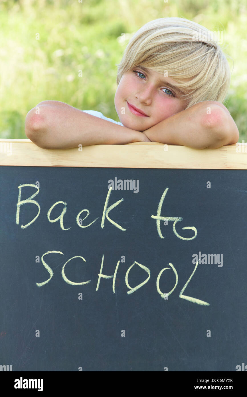 Niedliche Schuljunge stand neben der Tafel mit dem Text "back to School" Stockfoto