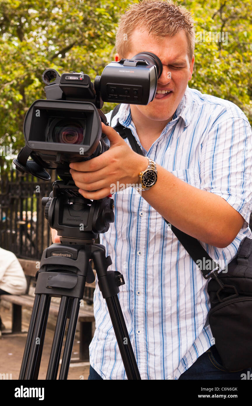 Ein Film-Kameramann mit seiner Videokamera auf einem kräftigen Manfrotto Stativ im Vereinigten Königreich Stockfoto