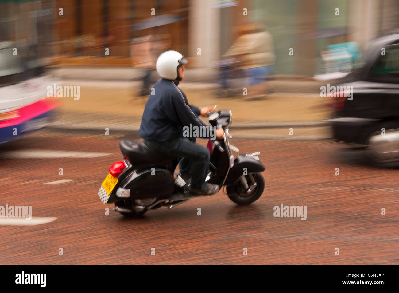 Ein Mann auf einem Roller fährt durch die Stadt und zeigt absichtlich Bewegungsunschärfe in Norwich, Norfolk, England, Großbritannien, Uk Stockfoto