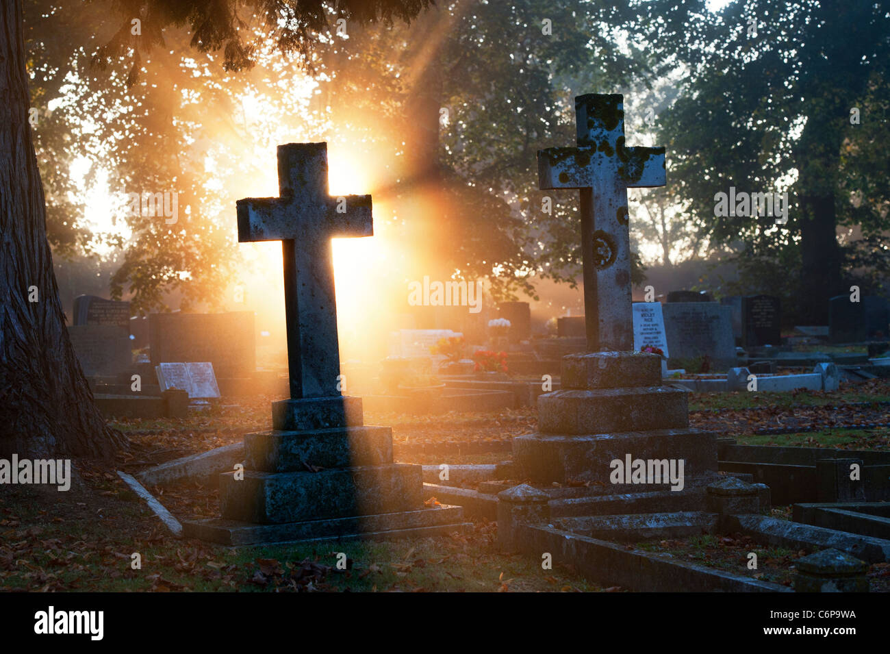 Friedhof Kreuz Grabsteine beleuchtet in der frühen Morgensonne durch Nebel. Kings Sutton, Northamptonshire, England Stockfoto