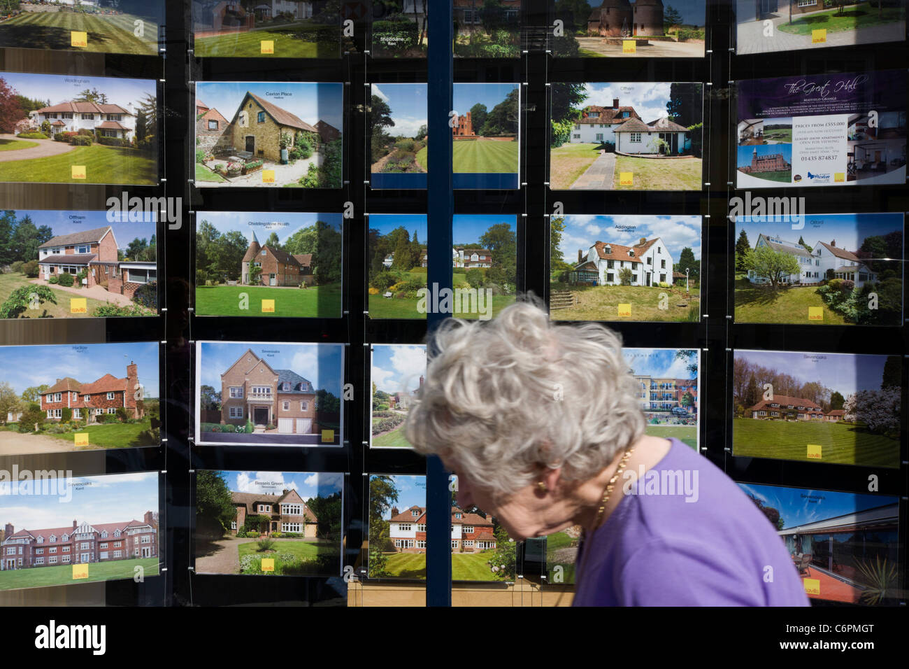 Ältere Dame geht Vergangenheit eine Reihe von Eigenschaften werden in einem Sevenoaks Immobilienmakler Hautpstraße Fenster angezeigt. Stockfoto