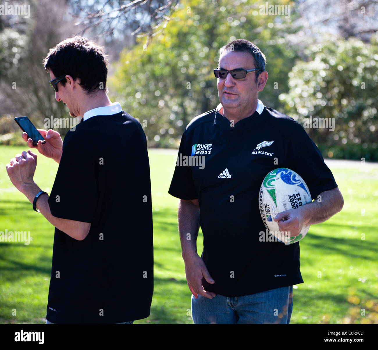 Zwei Rugby World Cup 2011 Unterstützer New Zealand All Blacks Hemden tragen. Ein Betrieb einen Souvenir World Cup Rugby-Ball. NZ Stockfoto