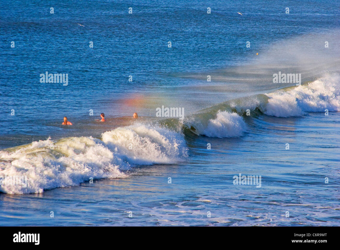 Drei Schwimmer in den Ozean jenseits der Brandung mit Regenbogen sichtbar in der Gischt Stockfoto