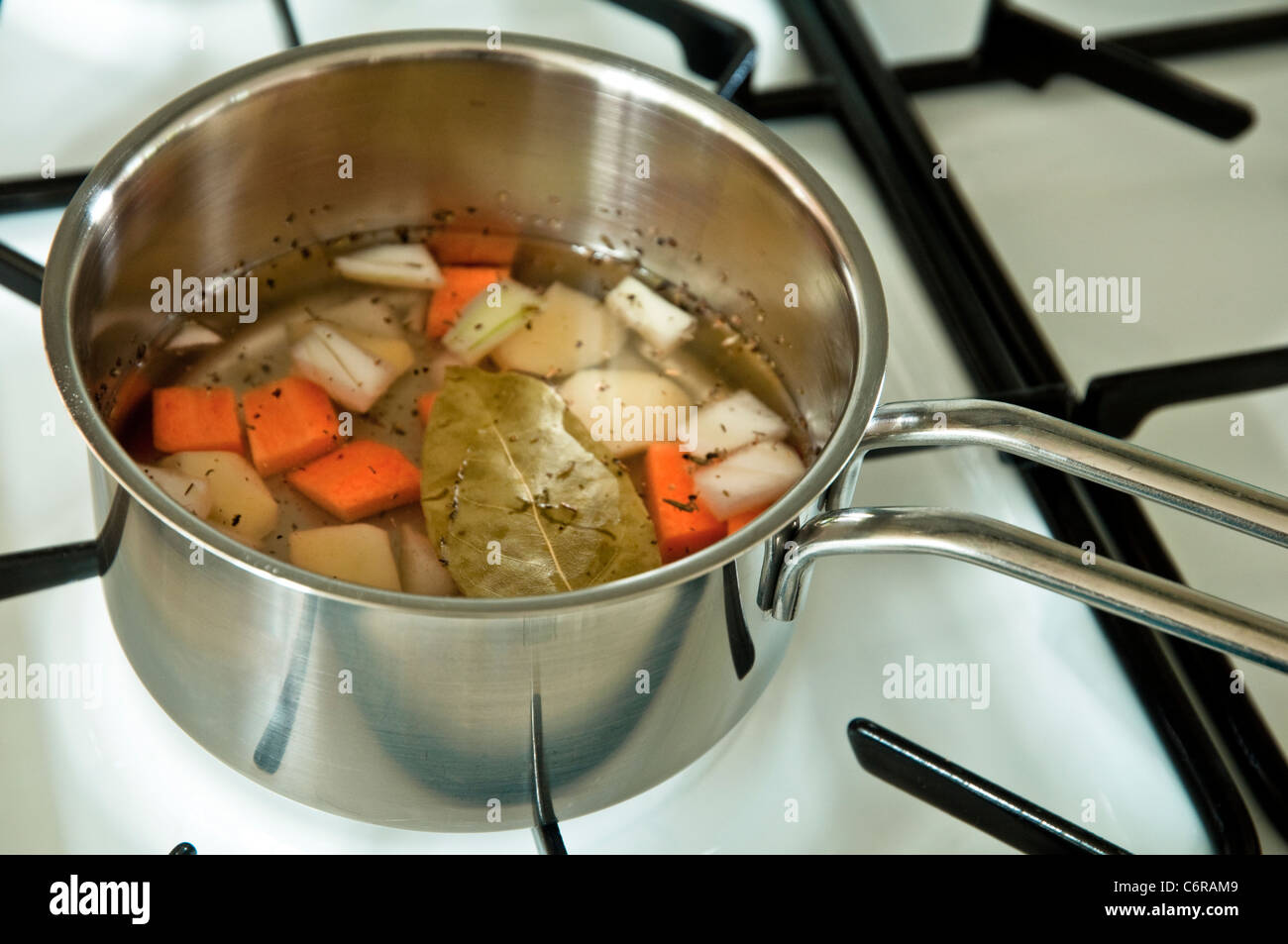 Machen eine Aktie (Grundlage für die Soße) in einer Pfanne auf dem Kochfeld mit einer Vielzahl von gehacktem Gemüse, Kräuter und Gewürze. Stockfoto