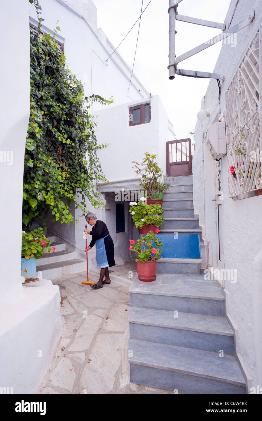 Griechische Frau fegt die Gasse vor ihrem Haus in Arnados auf der griechischen Kykladen Insel Tinos. Stockfoto