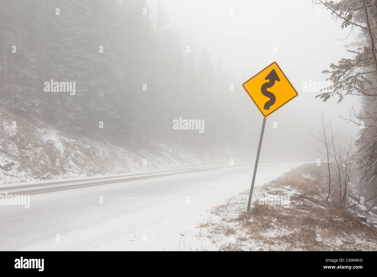 Eine gebogene Schild auf einer Bergstraße in Schnee und Nebel. Stockfoto