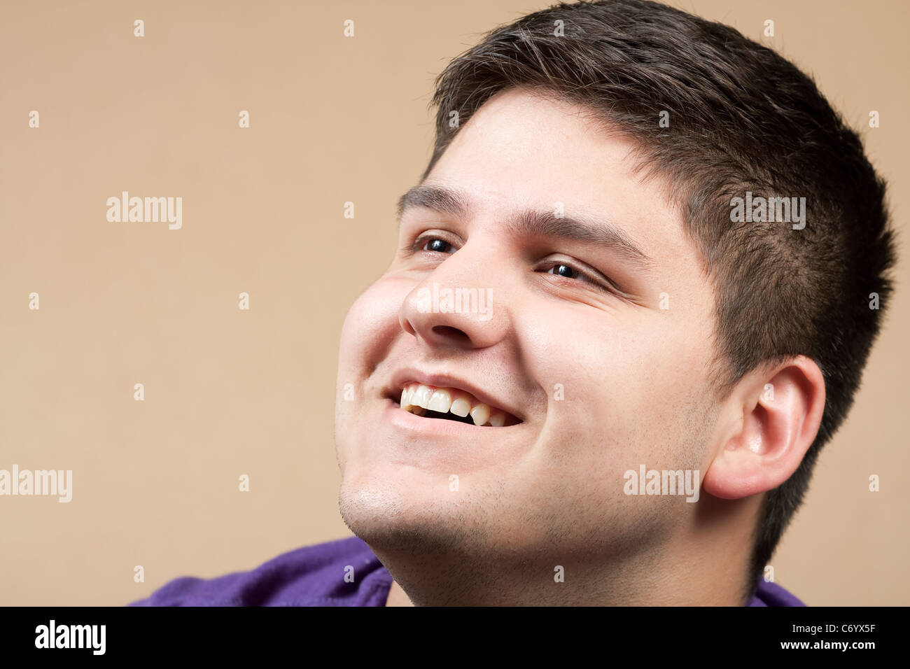 Ein lächelnder junger Mann in seinen späten Teenager über Tan farbigem Hintergrund isoliert. Stockfoto