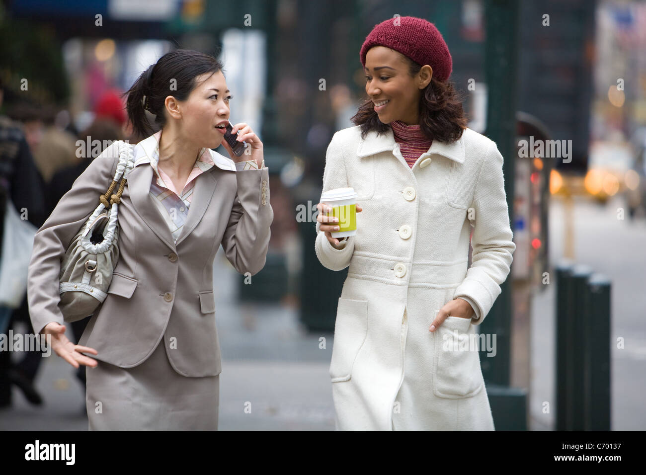 Zwei Business-Frauen in der großen Stadt zu Fuß. Man ist auf ihrem Handy. Stockfoto