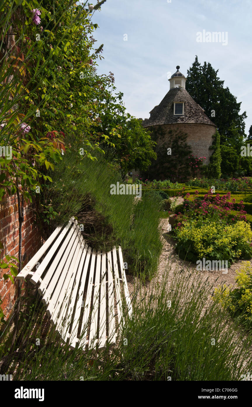 Eine stilvolle Gartenbank im Parterre Rousham Haus mit der ursprünglichen Taubenschlag darüber hinaus, Oxfordshire, England Stockfoto