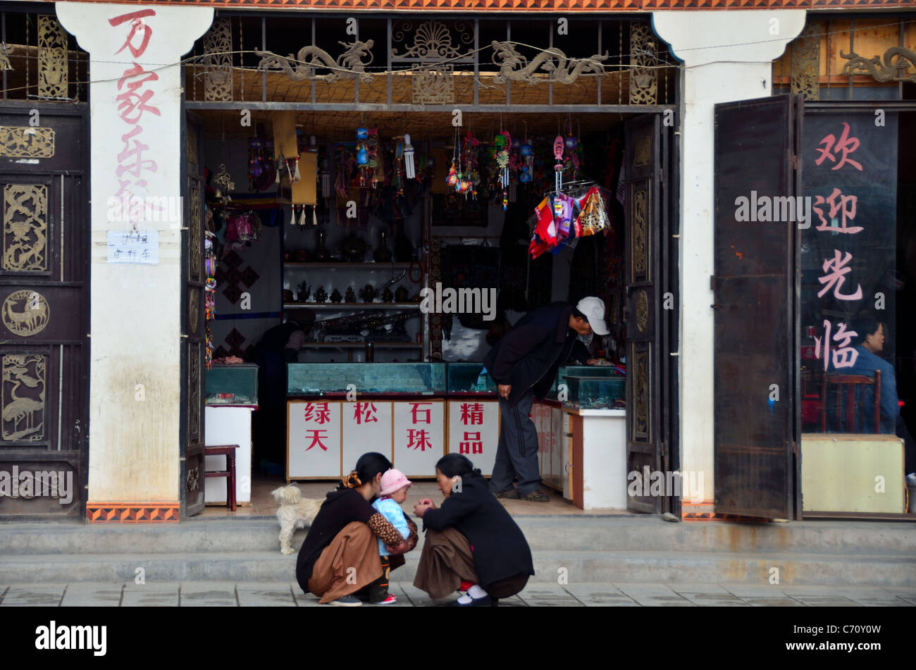 Zwei Frauen spielen mit einem Baby vor einem Geschäft im Daocheng. Sichuan, China. Stockfoto