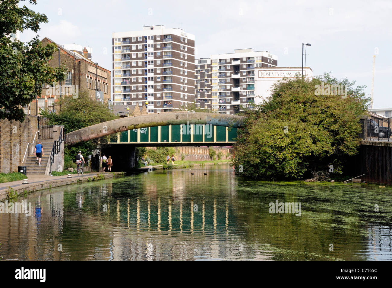 Brücke über die Regents Canal mit Menschen am Leinpfad und Wohnungen hinter Hackney London England UK Stockfoto