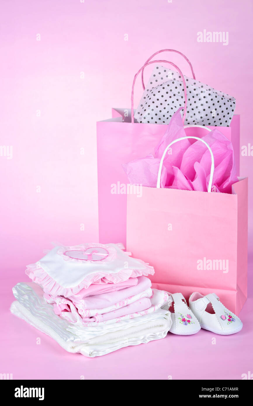 Geschenktüten und Baby-Kleidung für Mädchen-Baby-Dusche auf rosa Hintergrund Stockfoto