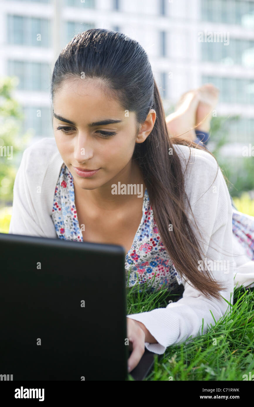 Junge Frau liegend auf Bauch auf Rasen mit laptop Stockfoto
