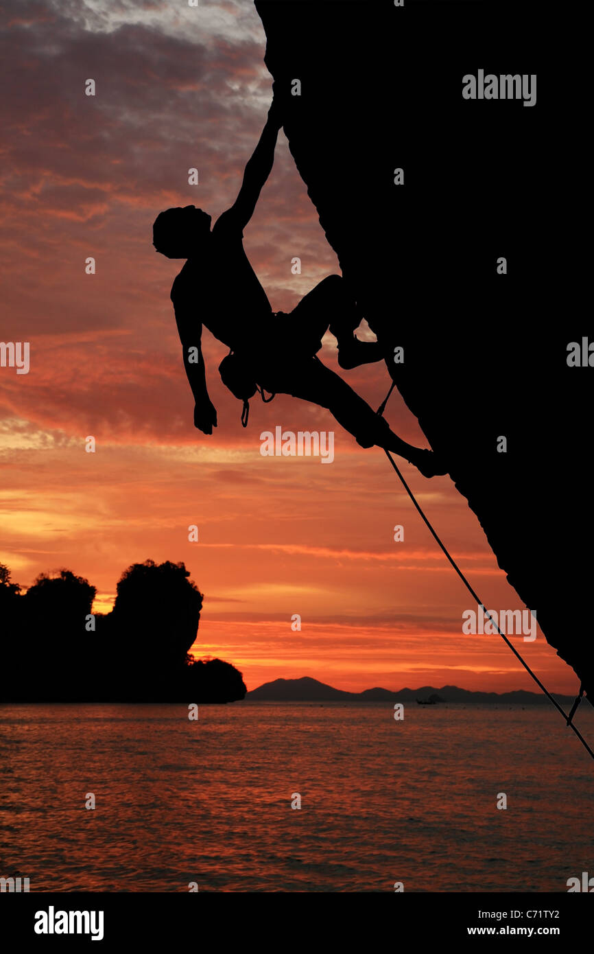 Silhouette der Kletterer Klettern einer überhängenden Felswand mit Sonnenuntergang über dem Ozean Hintergrund Stockfoto