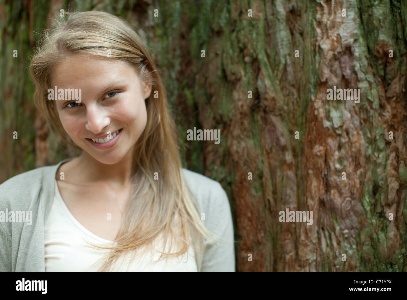 Junge Frau lehnt sich an Baumstamm, Porträt Stockfoto