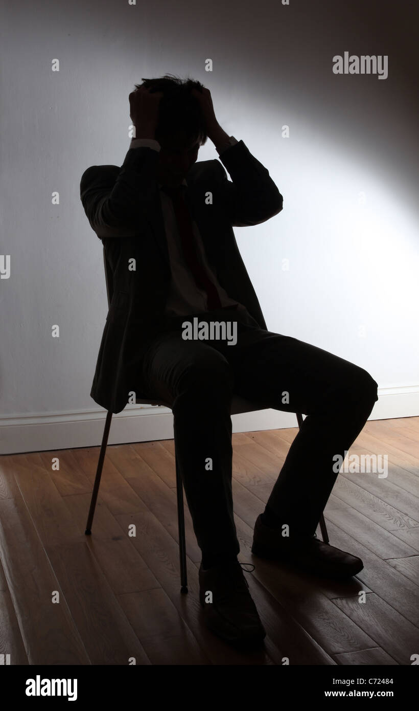 Silhouette von einem jungen Mann sitzt auf einem Stuhl, seine Haare herausreißen. Stockfoto