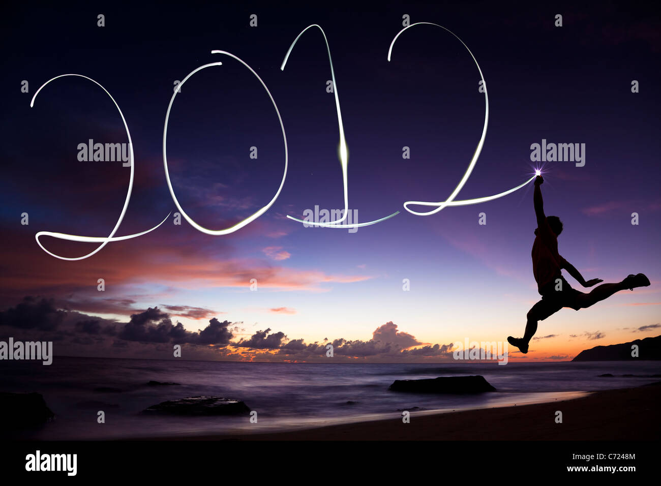 Frohes neues Jahr 2012. junger Mann springen und Zeichnung 2012 von Taschenlampe in der Luft am Strand vor Sonnenaufgang Stockfoto
