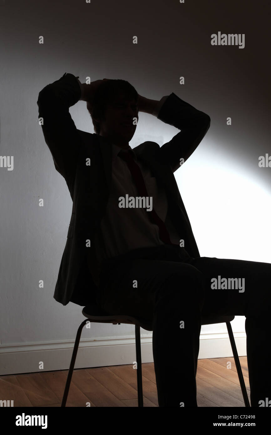 Silhouette von einem jungen Mann sitzt auf einem Stuhl mit den Händen hinter dem Kopf. Stockfoto