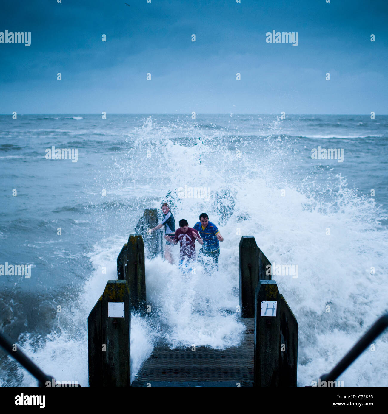riskieren ihr Leben - drei junge Leute, die die Wellen ausweichen, wie Stürme Aberystwyth an der Westküste von Wales getroffen. 11. September 2011 Stockfoto