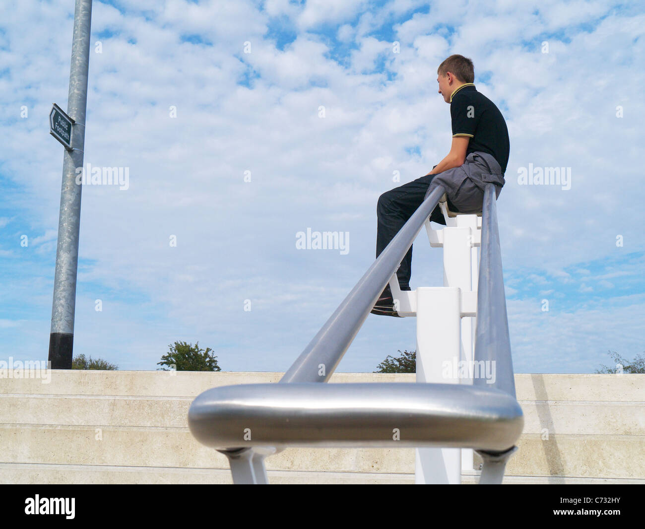 Junge saß und sah bei einem Wegweiser Stockfoto