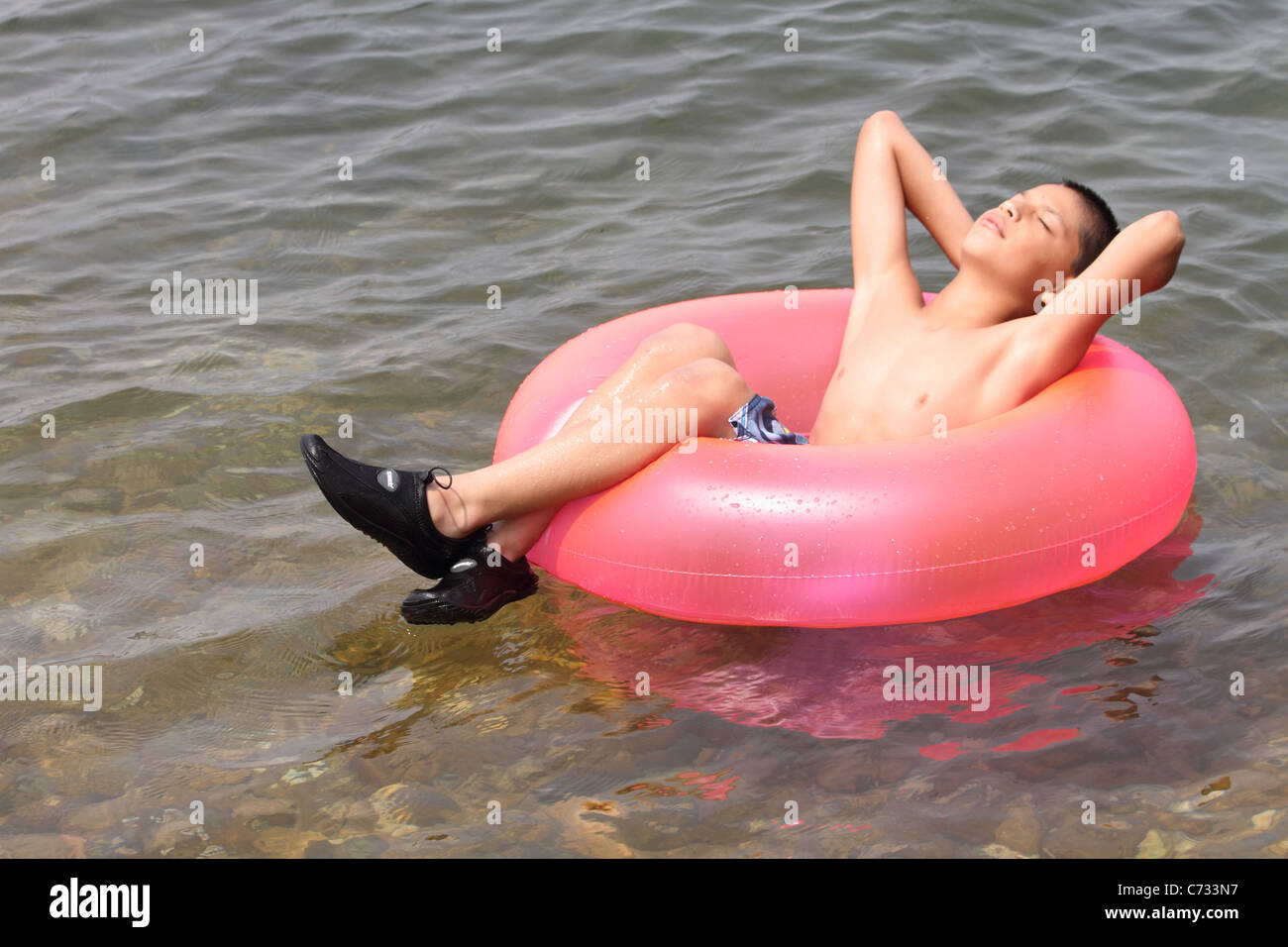 Junge auf Float Innenrohr im Ozean fangen Strahlen Stockfoto