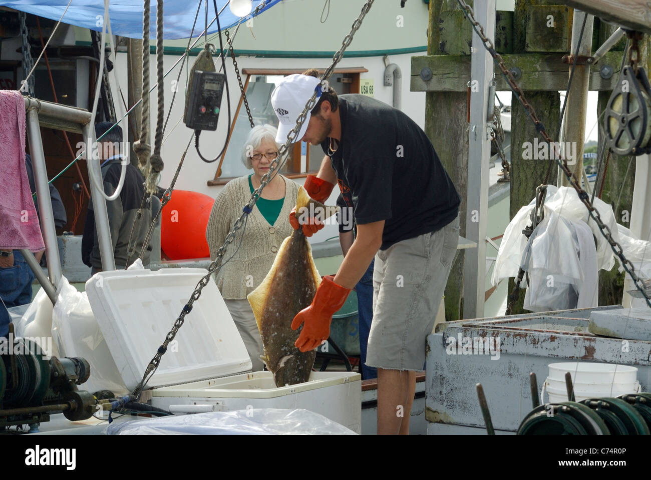 Kommerzielle Fischhändler hält einen frisch gefangenen Hailbut während eine Kundin schaut. Stockfoto