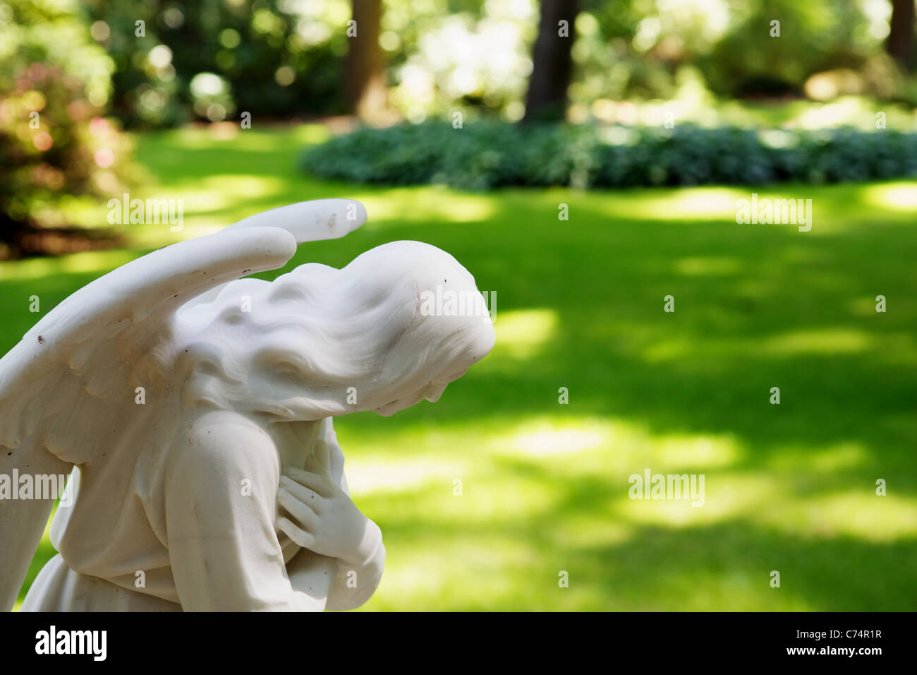 Skulptur eines Teils eines betenden Engels mit soft-Focus Park im Hintergrund Stockfoto