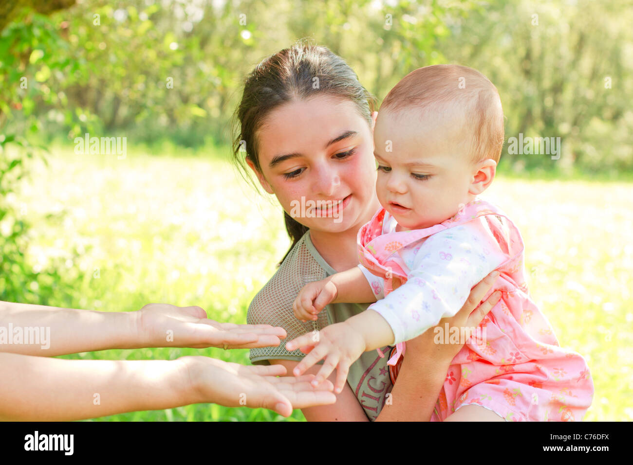 Ein Teenager mit einem Baby auf dem Arm geben dem Kind zur Mutter Stockfoto