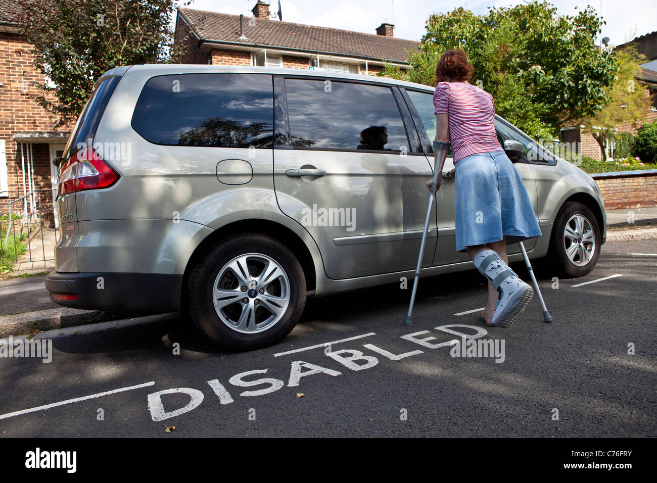 Frau mit gebrochenem Bein entsperren Autotür geparkt deaktiviert, Parkplatz. Stockfoto