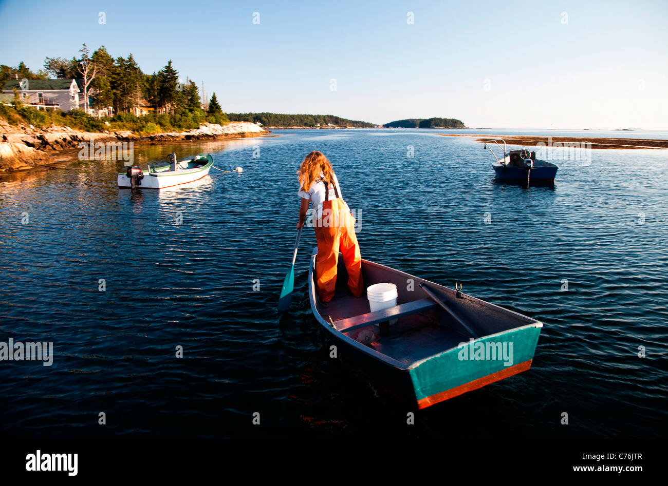 Eine Frau paddelt ihr Boot in einem kleinen Hafen bei Sonnenuntergang, nachdem sie Hummer aus Unterwasser fallen vor der Küste gesammelt hat. Stockfoto