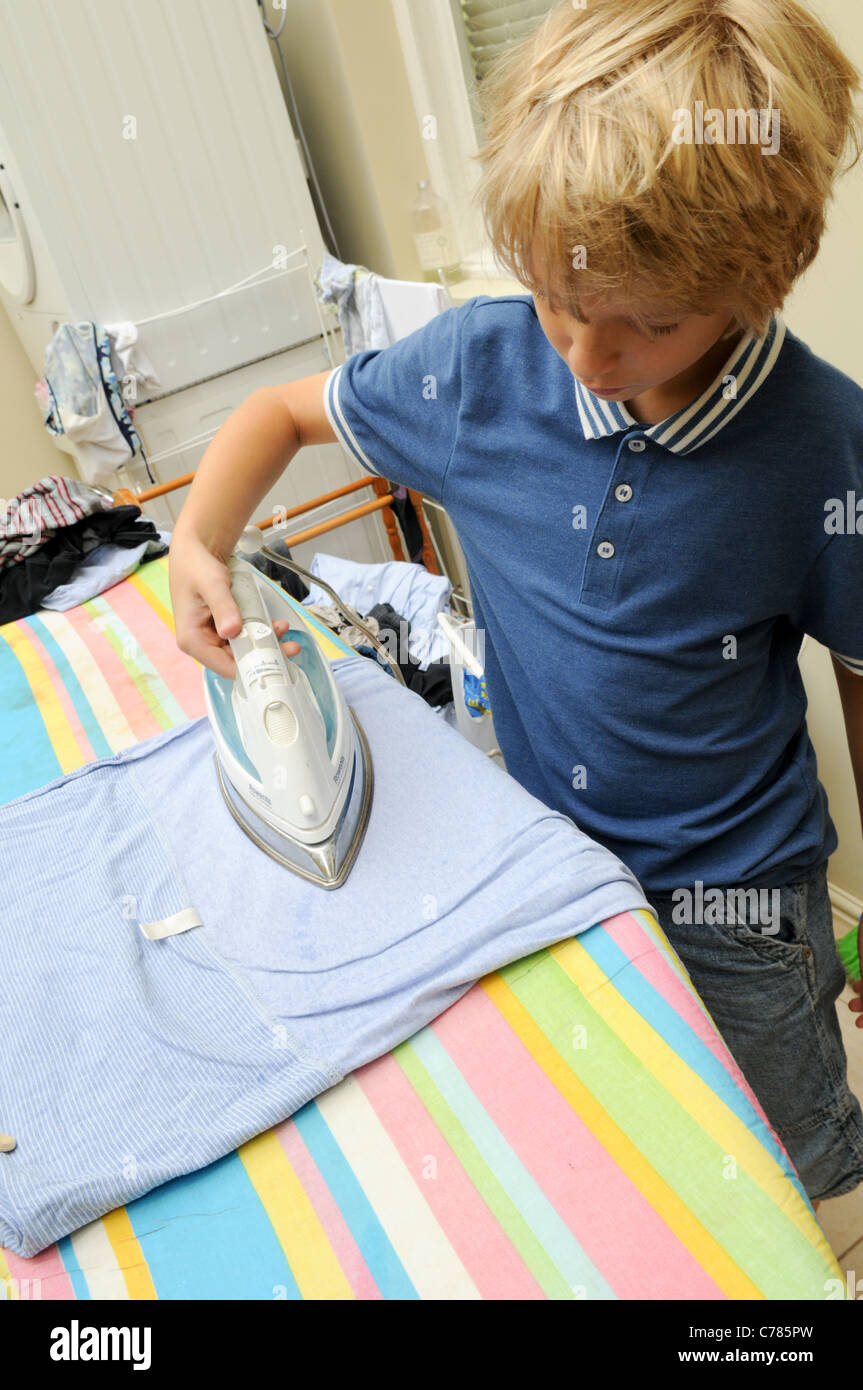 Blonde Junge konzentriert sich das Lernen auf ein Brett in einer Waschküche, einem heißen elektrischen Naht Eisen zu Eisen Stockfoto