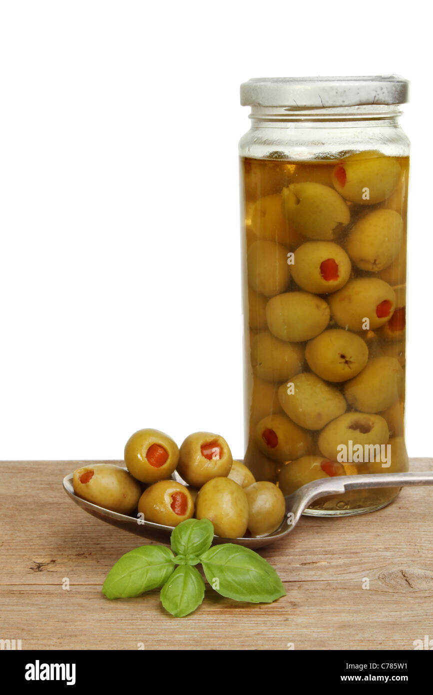 Oliven in einem Löffel mit ein Glas mit Oliven und Basilikum Kraut auf einem alten Holzbrett Stockfoto