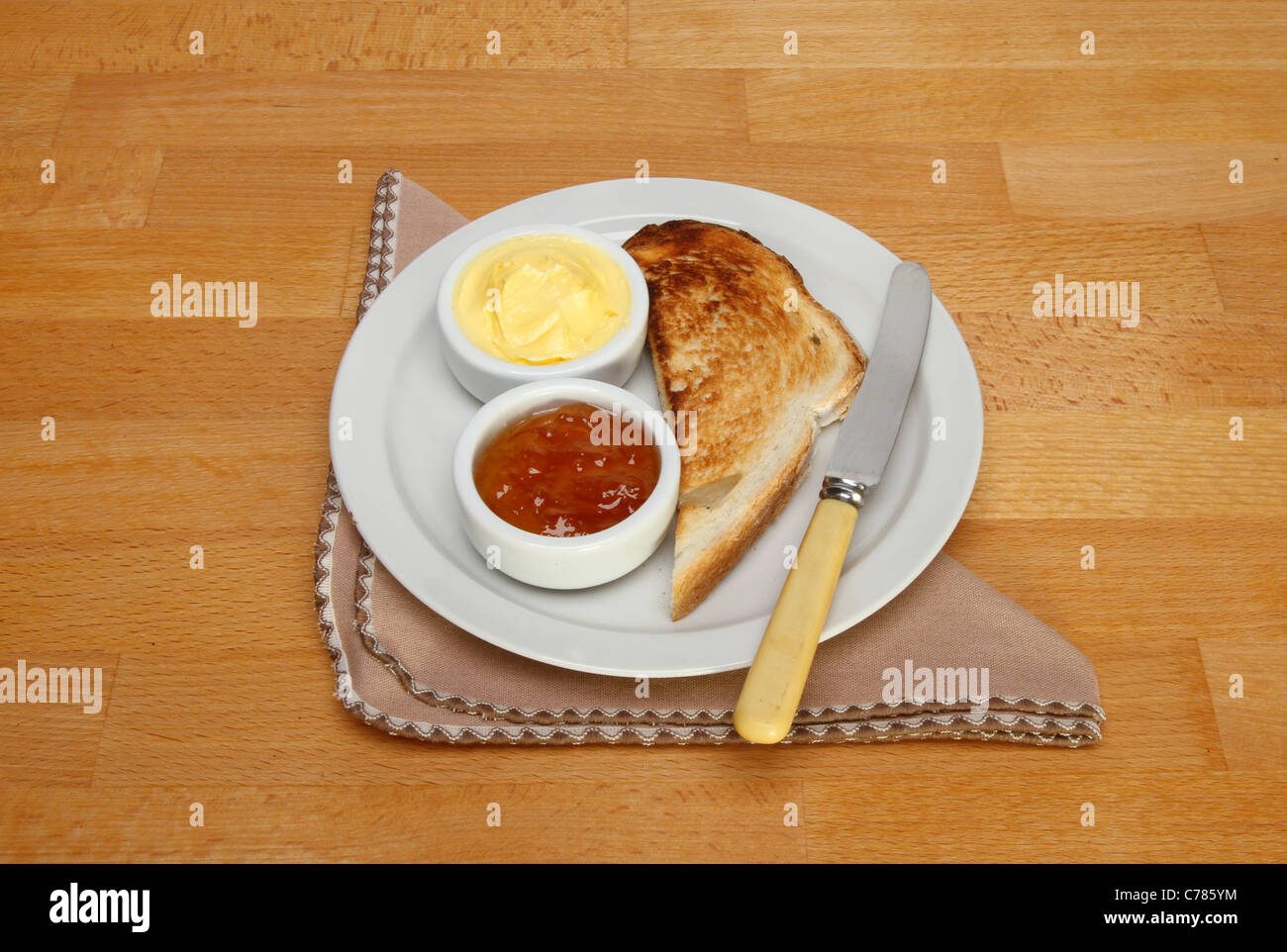 Toast, Marmelade und Butter auf einem Teller mit Messer und Serviette auf einem Holztisch Stockfoto