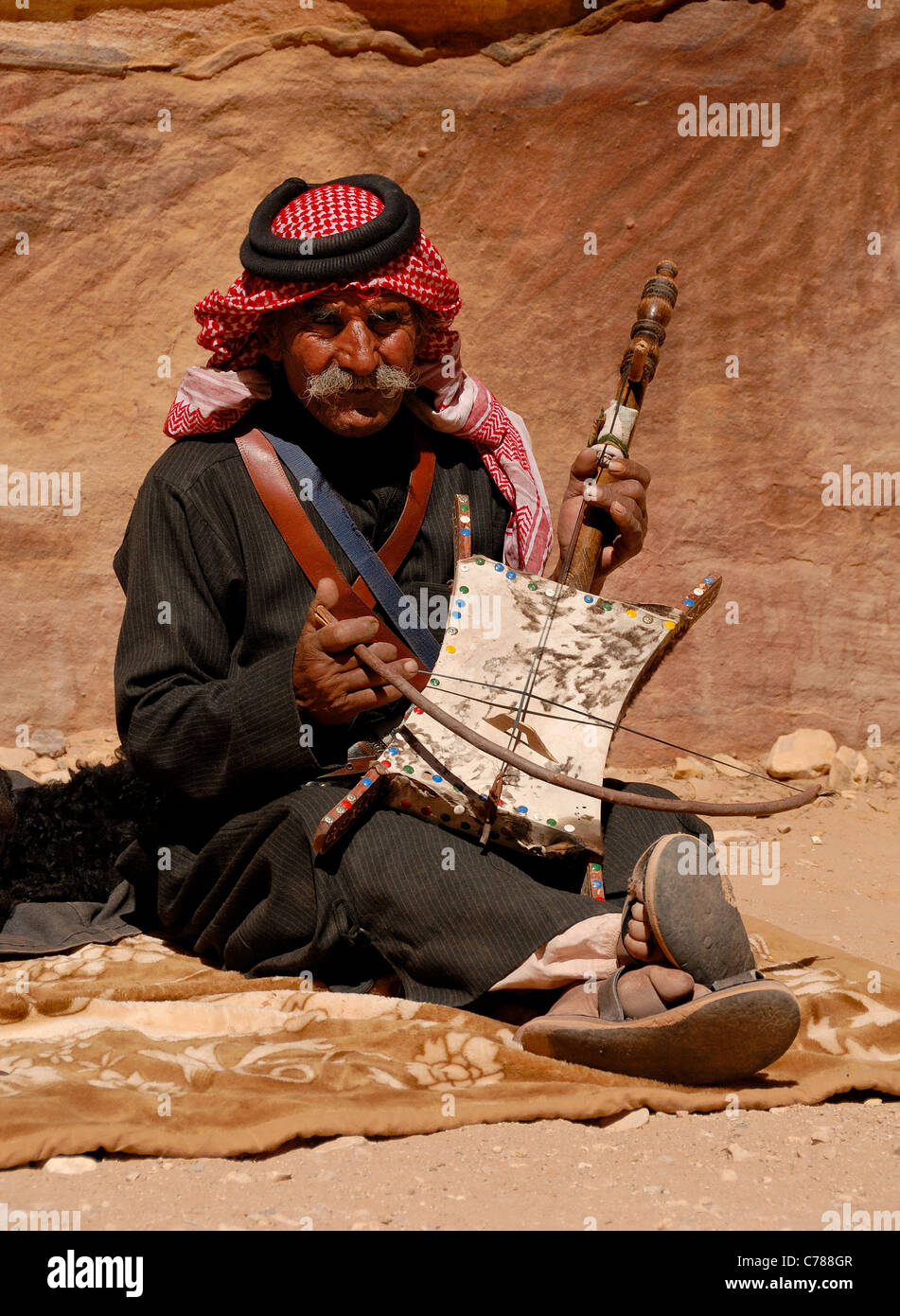 Alten Beduinen Mann Ssitting in der steinernen Stadt Petra und spielte eine Melodie auf seinem Instrument etwas archaisch. Stockfoto